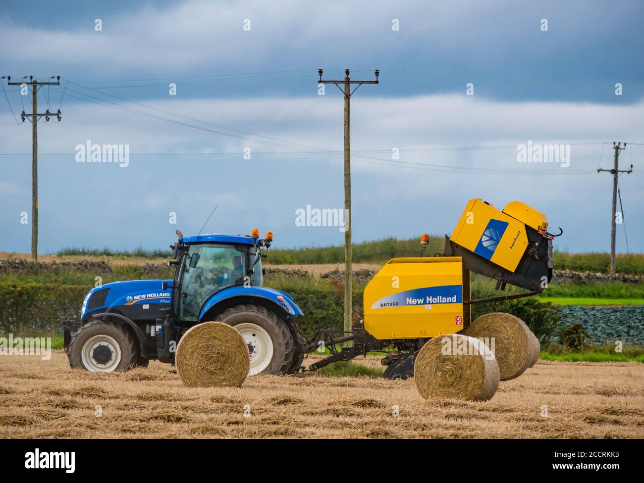Operatore agricolo che guida il trato con l'imballatrice per fieno nel campo di coltura, East Lothian, Scozia, Regno Unito Foto Stock