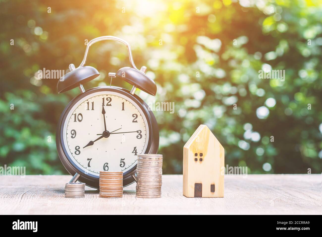 Primo piano, modello di casa di denaro e orologio con sfondo verde bokeh, concetto di risparmio di denaro per prepararsi per il futuro. Foto Stock