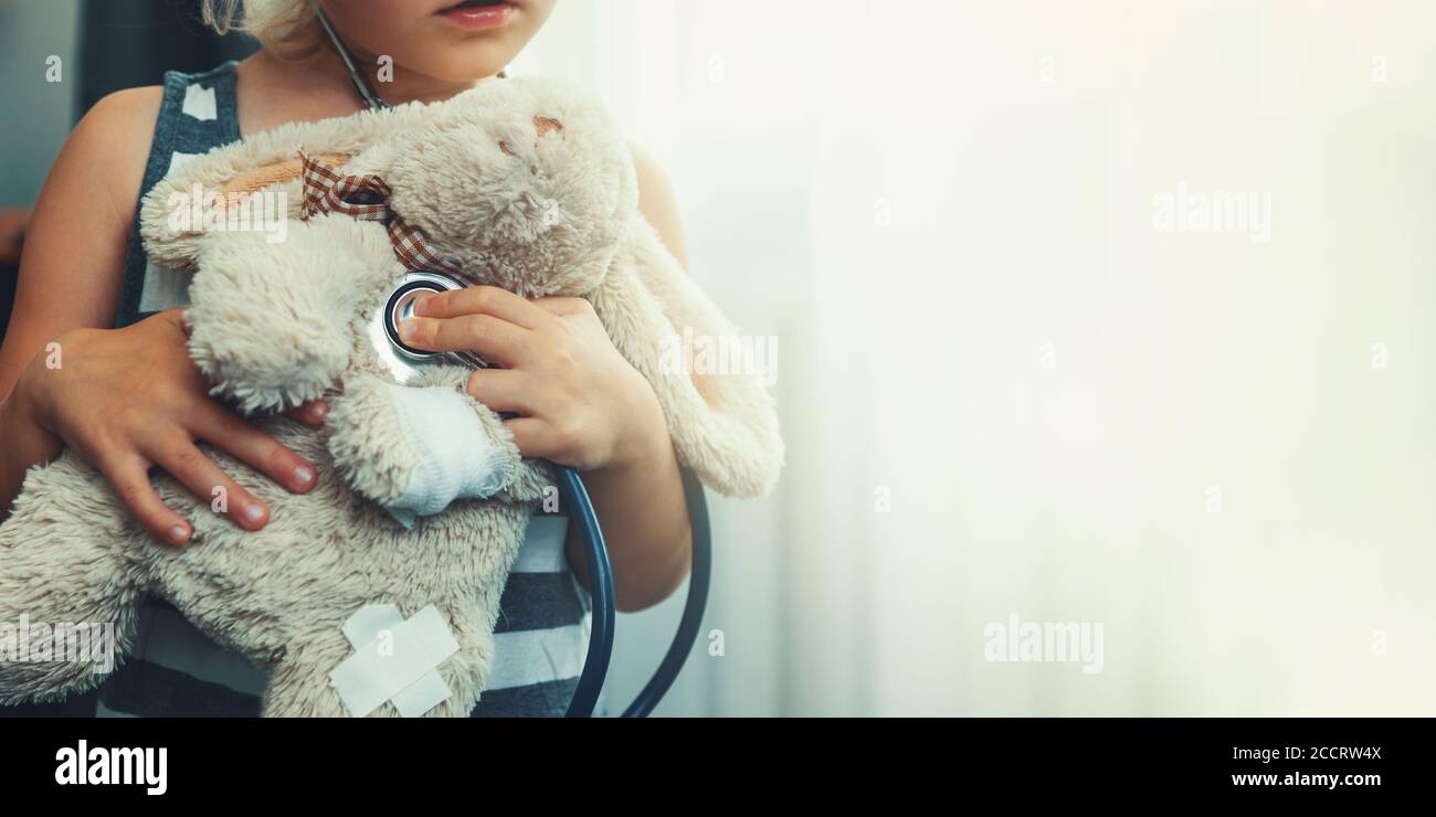 bambino che gioca medico con giocattolo morbido. ragazza che esamina coniglietto con stetoscopio. copia spazio Foto Stock