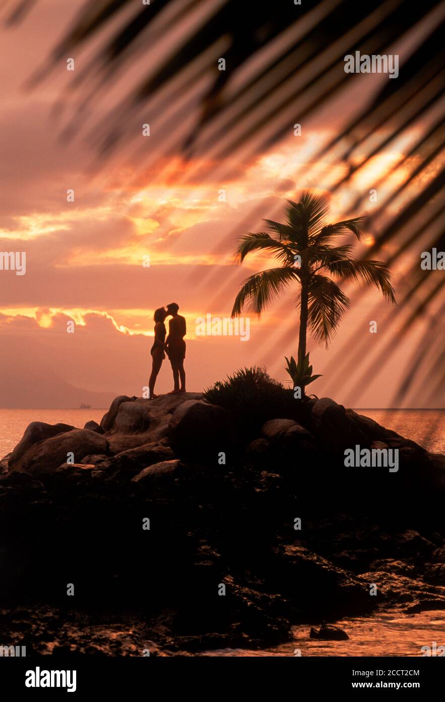 Coppia su una piccola isola con palme soleggiate al tramonto Sull'isola di Mahe alle Seychelles Foto Stock