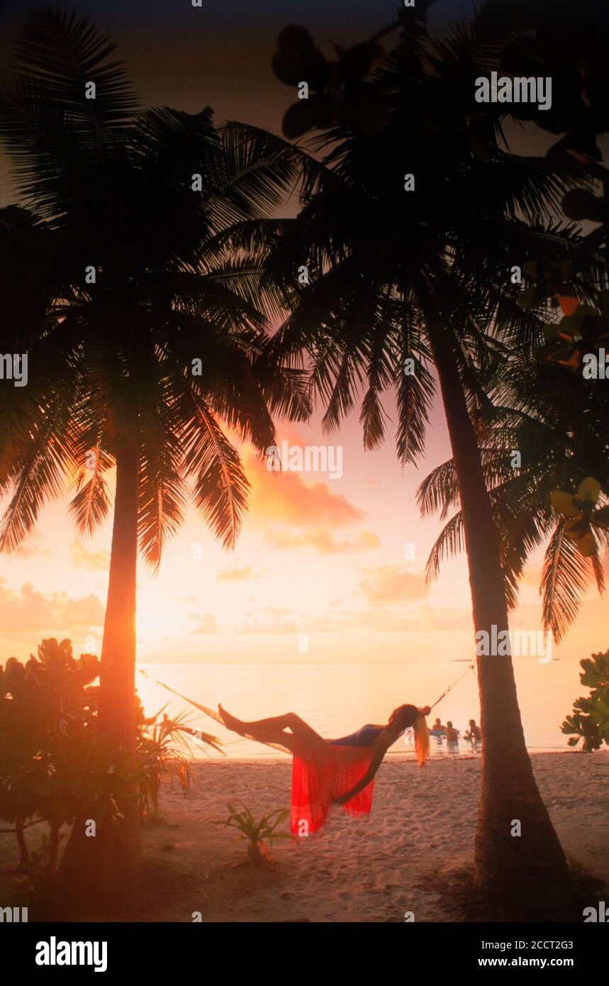 Donna in amaca tra palme in vacanza isola tropicale silhouette alla luce del tramonto Foto Stock