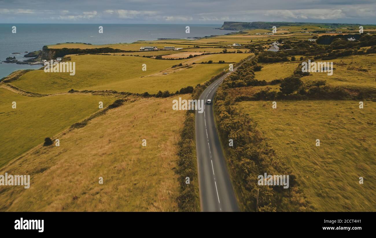 Strada aerea autunnale: Vista del viaggio in auto. Bella campagna dell'Irlanda del Nord scena naturale con strada contro la scogliera atlantica costa in tonalità di giallo autunno Foto Stock
