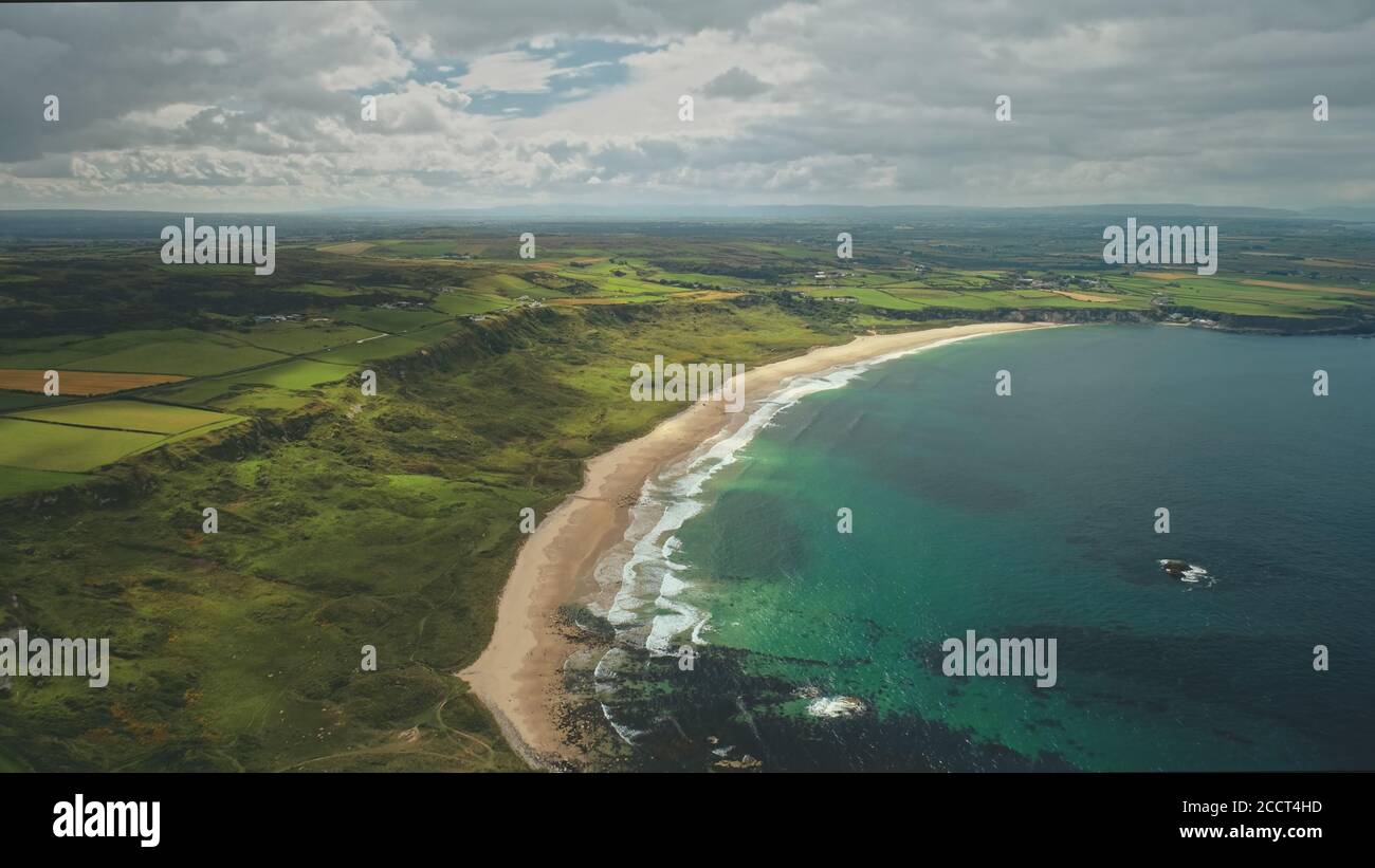 Panorama panoramico della spiaggia nella contea di Antrim, Irlanda del Nord. La splendida costa dell'Oceano Atlantico, i verdi prati e la campagna si estendono fino alle nuvole grigie. Foto Stock