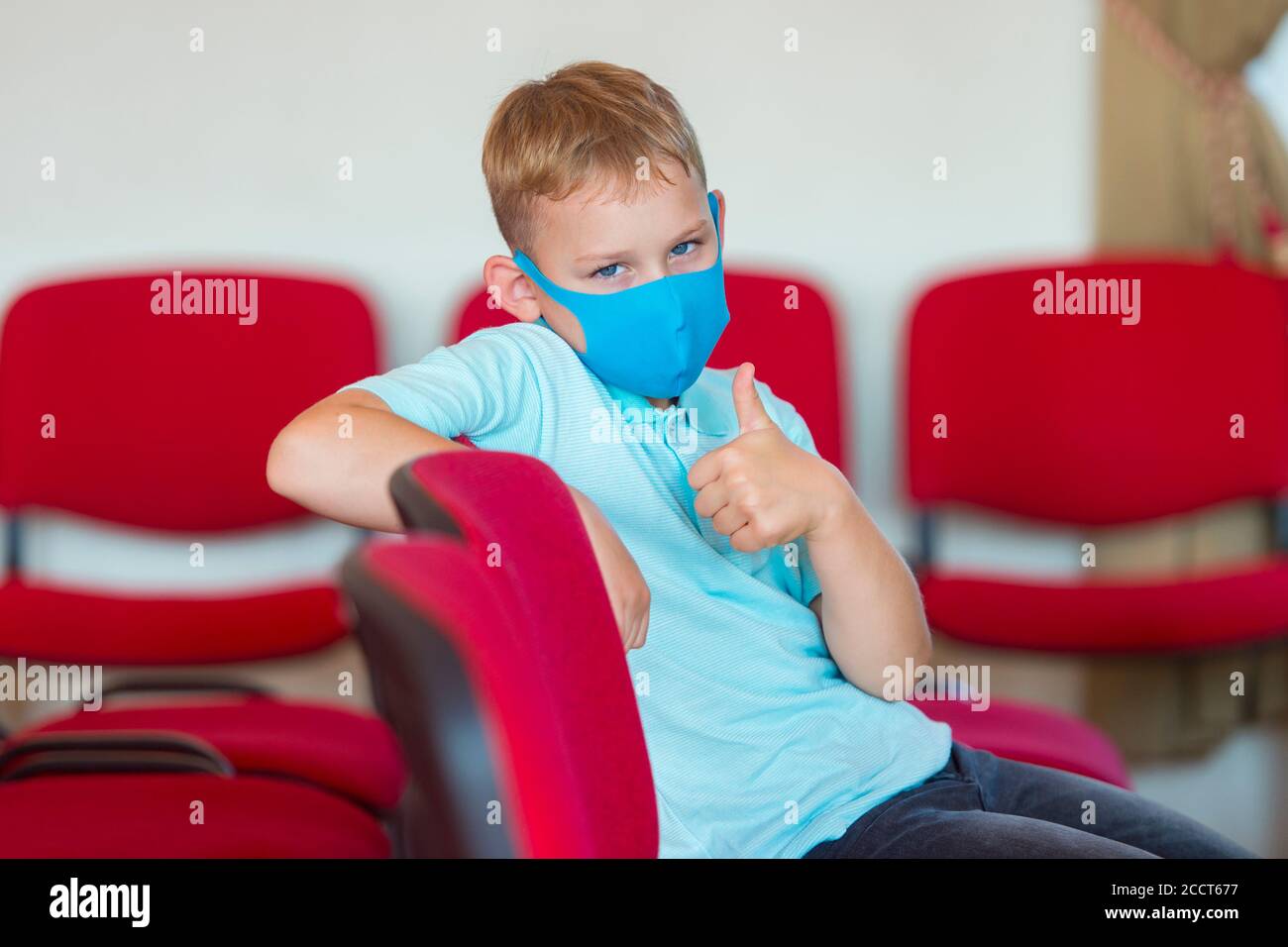 Il bambino della scuola con la maschera blu contro il virus mostra sulle dita un segno alla lezione e all'evento. Ritorno sicuro a scuola durante il concetto pandemico. Divaricare sociale Foto Stock