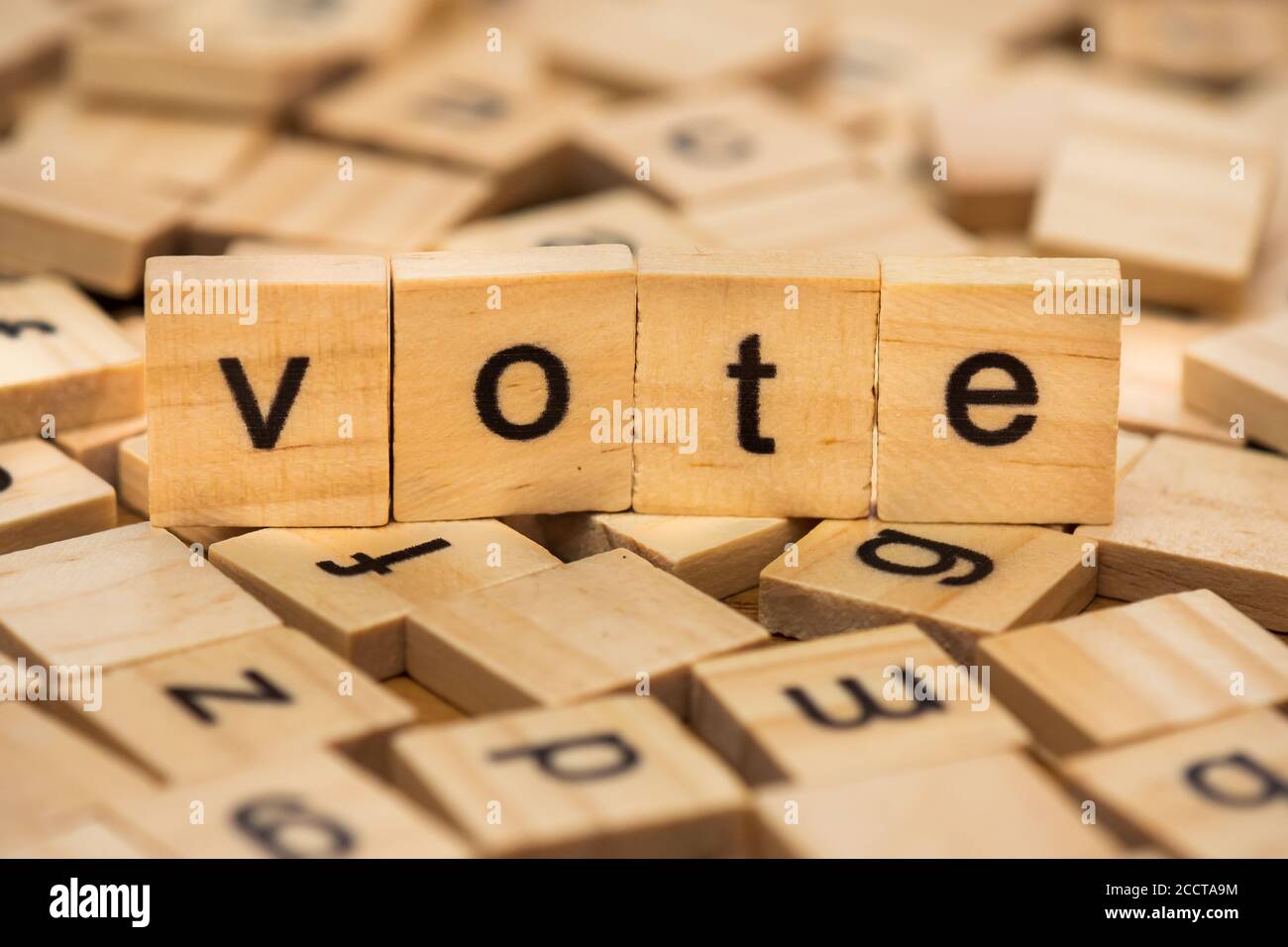 Lettere di legno che compongono la parola 'voto' su uno sfondo di lettere sparse versate su una tavola di legno Foto Stock