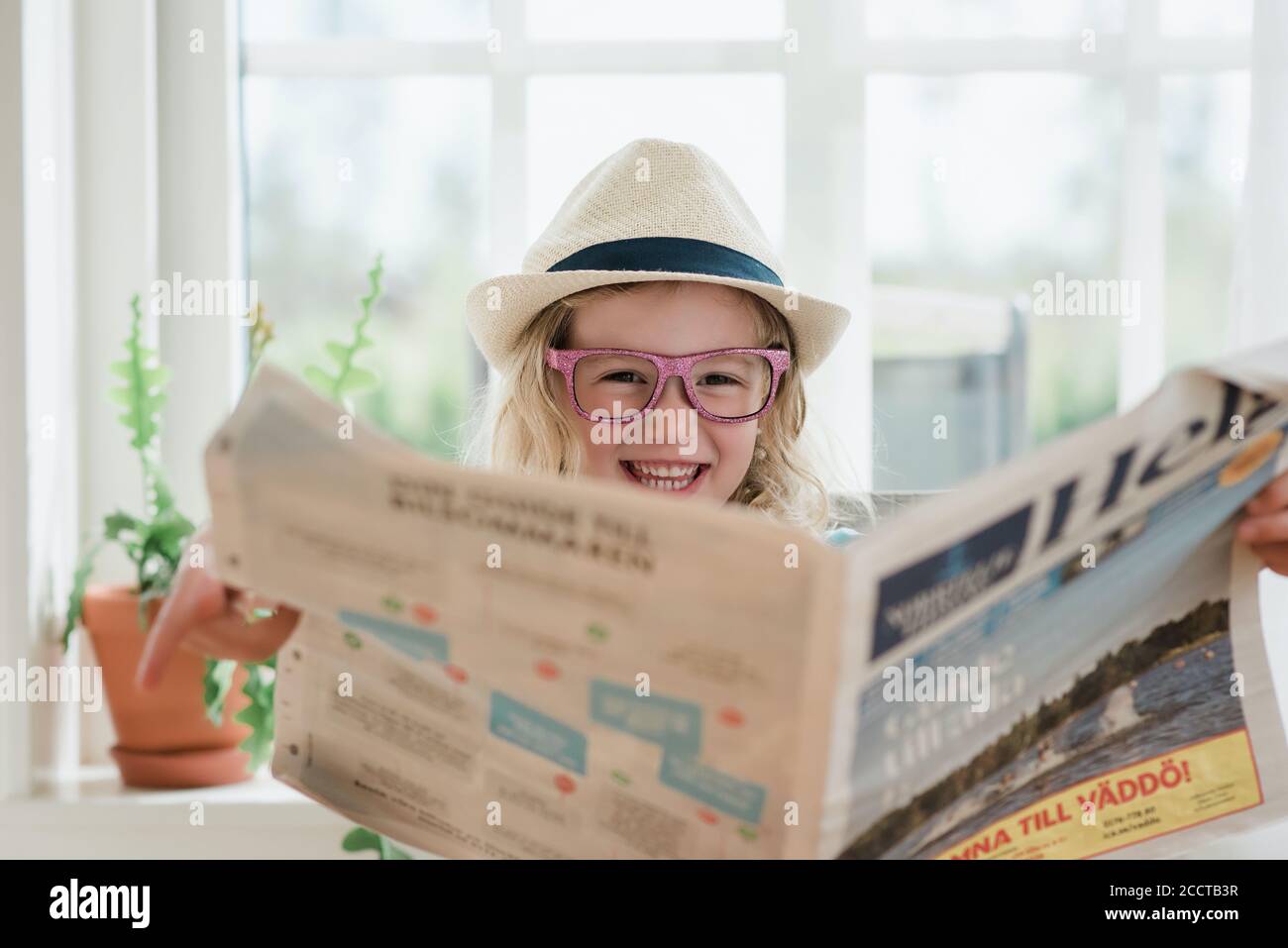 giovane ragazza che ride mentre legge un giornale con un cappello e  bicchieri Foto stock - Alamy