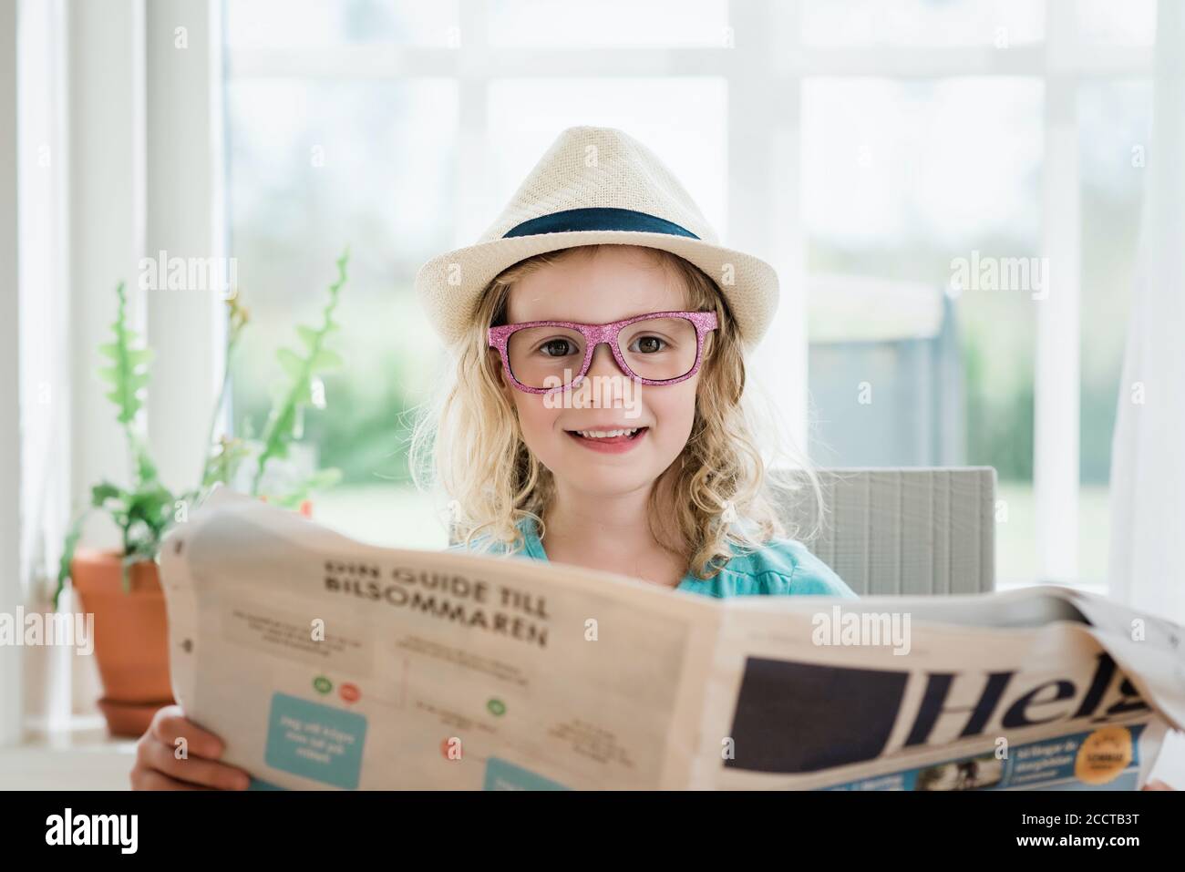 giovane ragazza che legge un giornale con un cappello e bicchieri essere  divertente Foto stock - Alamy