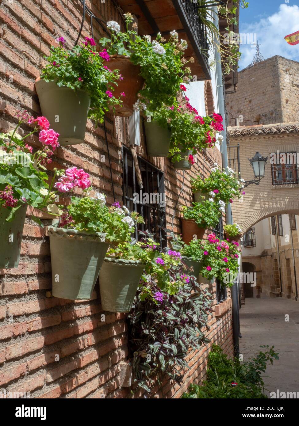 Vasi di fiori con fiori colorati appesi da un muro di mattoni In un  villaggio spagnolo Foto stock - Alamy