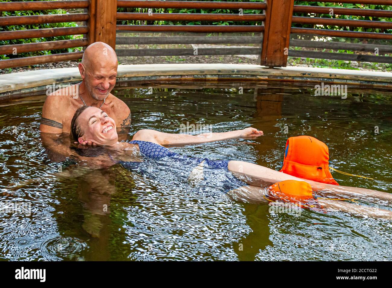 Haki-Flow allevia la tensione al collo e alle spalle nell'acqua termale calda. Il terapista Antonio Ventura sorride mentre guida la giornalista Angela Berg, sostenuta da galleggianti per le braccia, attraverso la piscina termale dell'Hotel Adler Thermae a Bagno Vignoni, Val d'Orcia, Italia, con movimenti serpenteggianti. Foto Stock