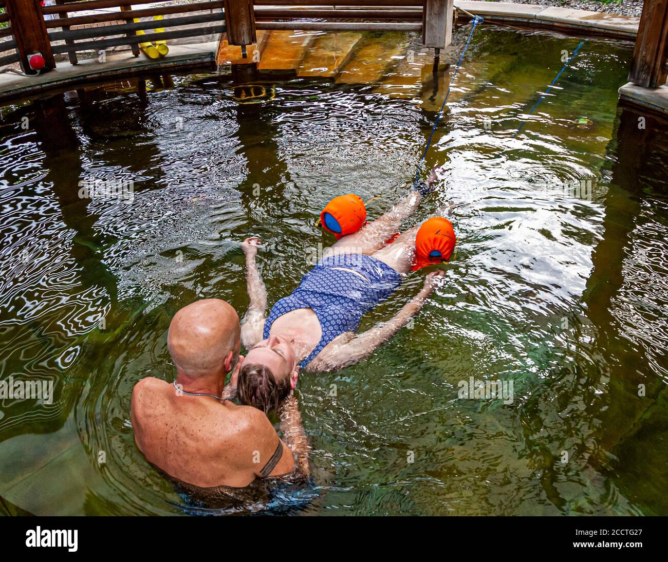 Haki-Flow allevia la tensione al collo e alle spalle nell'acqua termale calda. Il terapista Antonio Ventura guida la giornalista Angela Berg, sostenuta da galleggianti per le braccia, attraverso la piscina termale rotonda con struttura in legno dell'Hotel Adler Thermae a Bagno Vignoni, Val d'Orcia, Italia, con movimenti simili a quelli di un serpente. Foto Stock