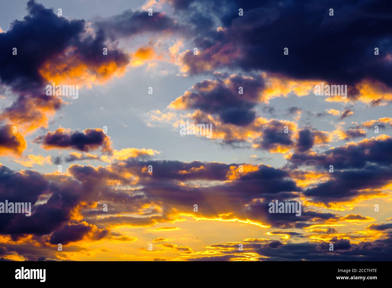 Un cielo molto drammatico pieno di gialli, blu e arance. Nuvole a contrasto durante il tramonto illuminate dal sole che tramonta. Naturale saturo luminoso Foto Stock