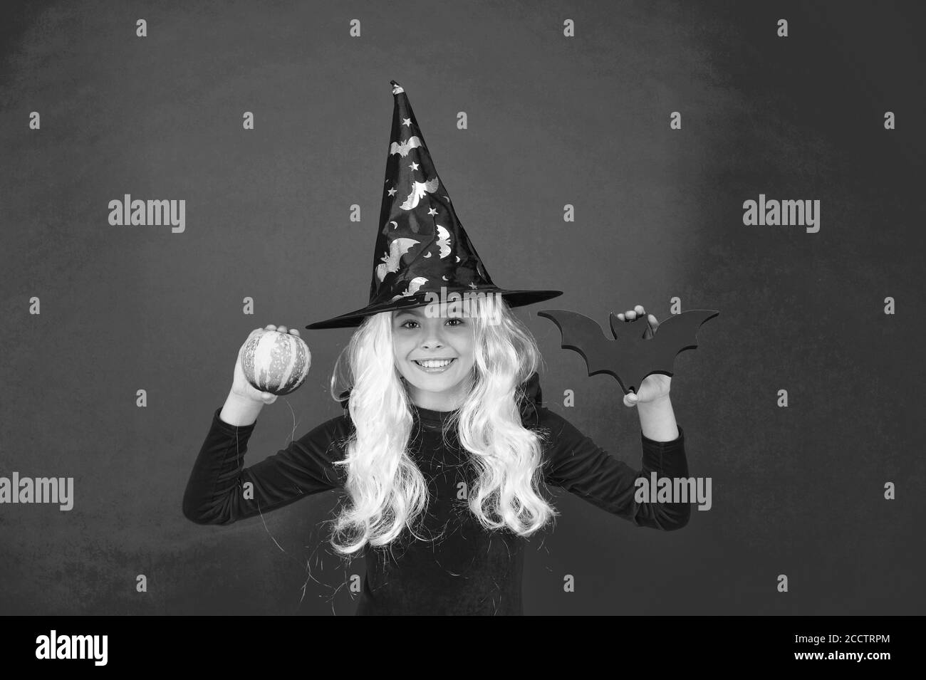 Spaventare la fabbrica. Ragazza strega tenere bat e zucca. Piccola Ragazza strega usura hat e capelli. Piccola ragazza con il look di Halloween. Festa di Halloween girl pink background. Foto Stock