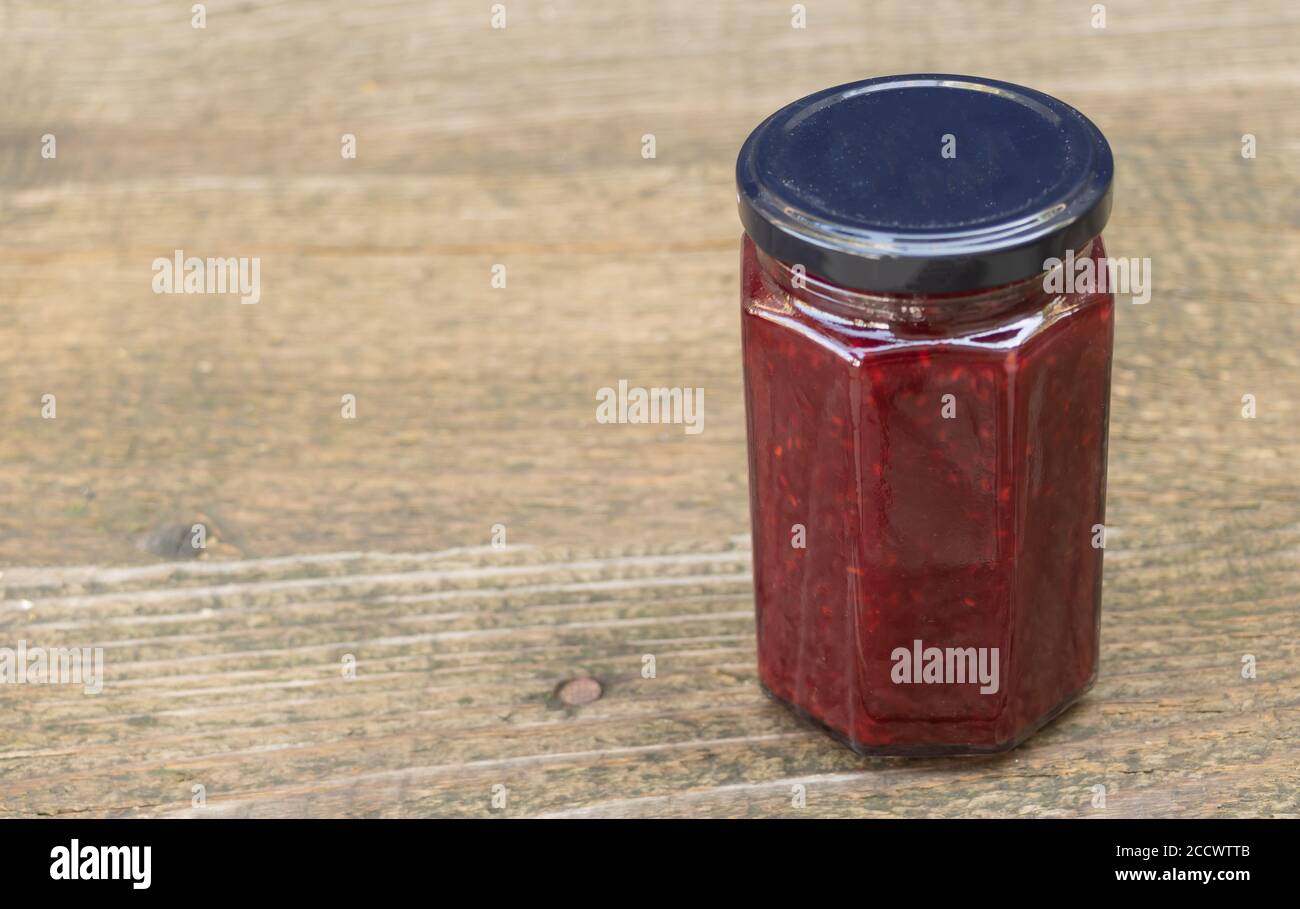 Un vasetto di confettura di lamponi su sfondo di legno. I vantaggi della marmellata di lamponi Foto Stock