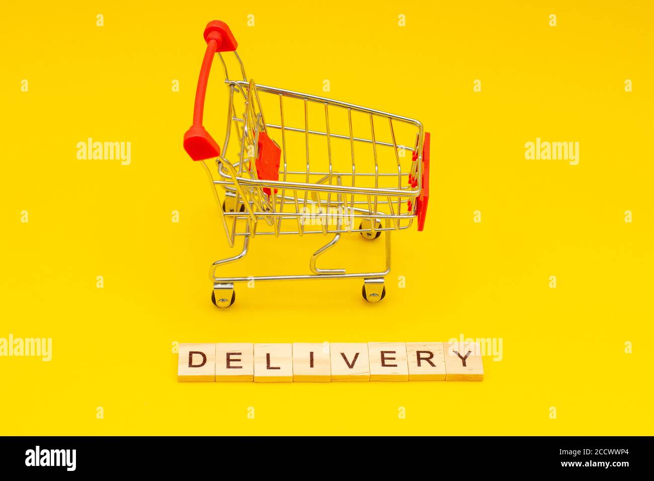 Consegna parola fatta da cubetti di legno su sfondo giallo con carrello giocattoli Foto Stock