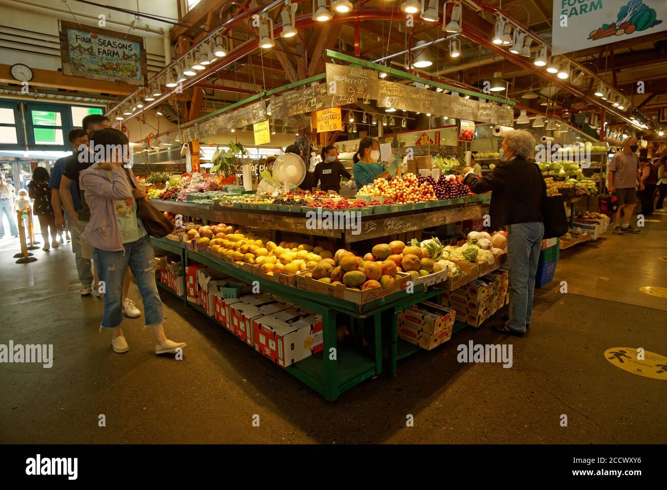 Le persone che indossano maschere di protezione che acquistano frutta e verdura da un fornitore di prodotti al Granville Island Market, Vancouver, BC, Canada Foto Stock