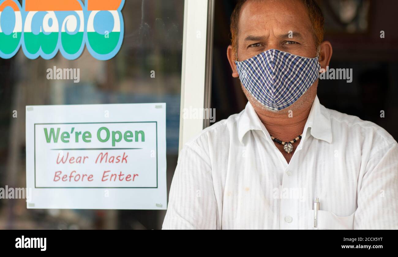 Proprietario di piccola impresa in maschera medica in piedi di fronte porta con noi siamo aperti maschera di usura scheda di avviso - concetto di sostegno comunità locale e acquistare Foto Stock