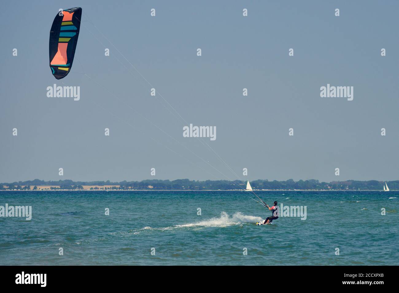 Bruna donna kitesurf o kite boarding che si allontana dal spiaggia di sabbia che fa per acque più profonde in un'estate soleggiata giorno in una vista posteriore del venuto Foto Stock