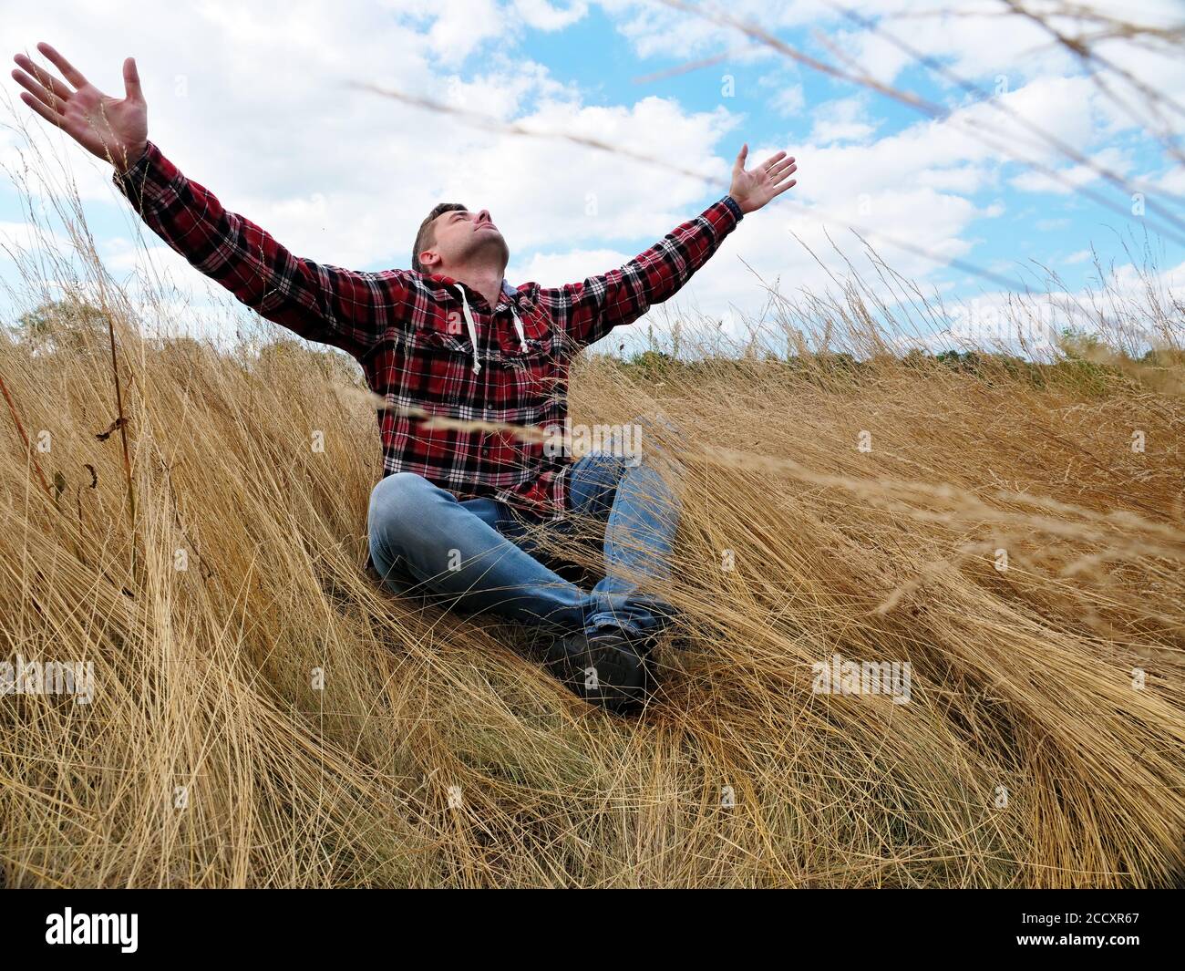 L'uomo calmo distende le mani verso il cielo mentre si siede in natura. Relax e consapevolezza. Foto Stock
