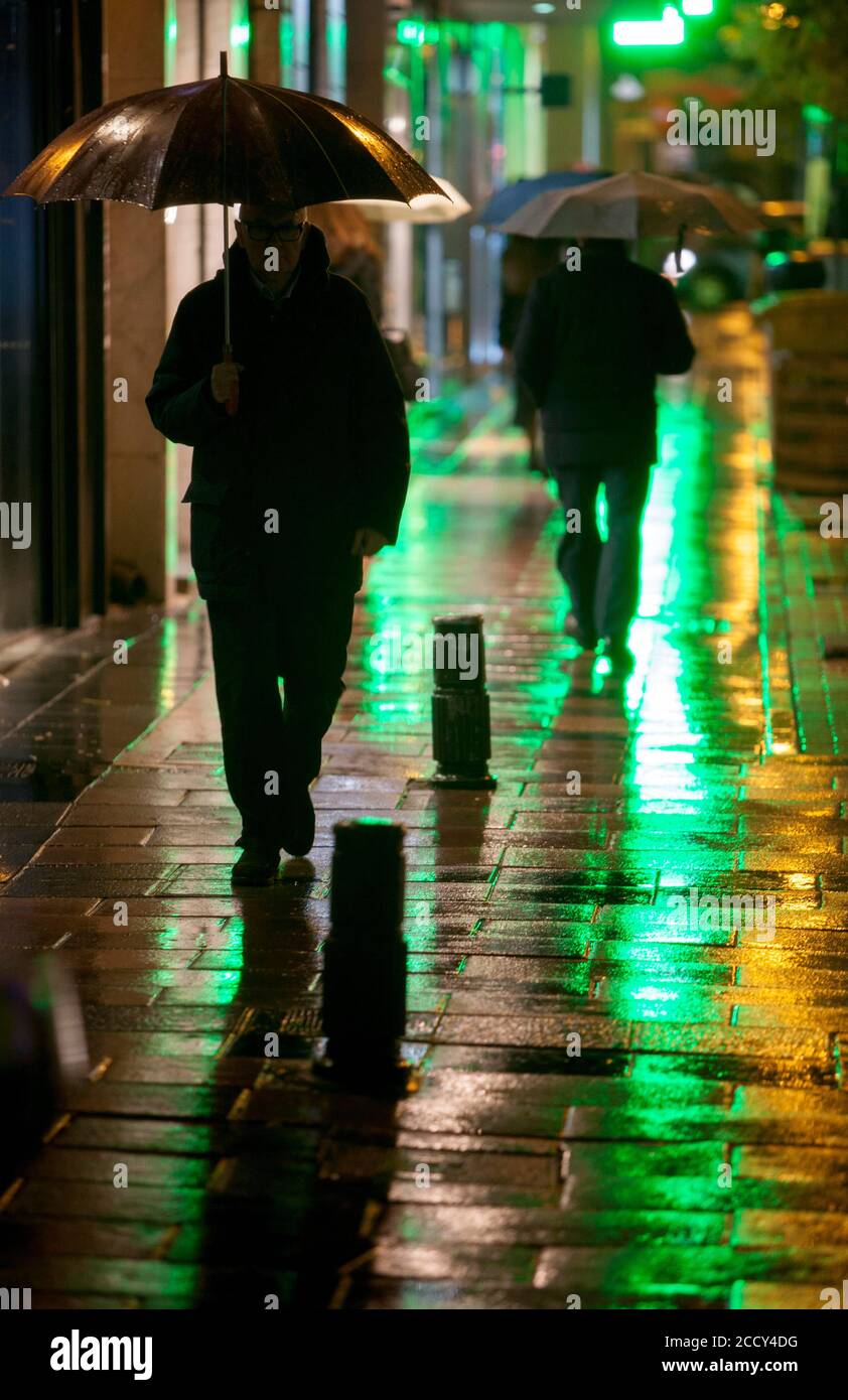 La gente cammina sotto la pioggia in una strada commerciale di Madrid Foto Stock