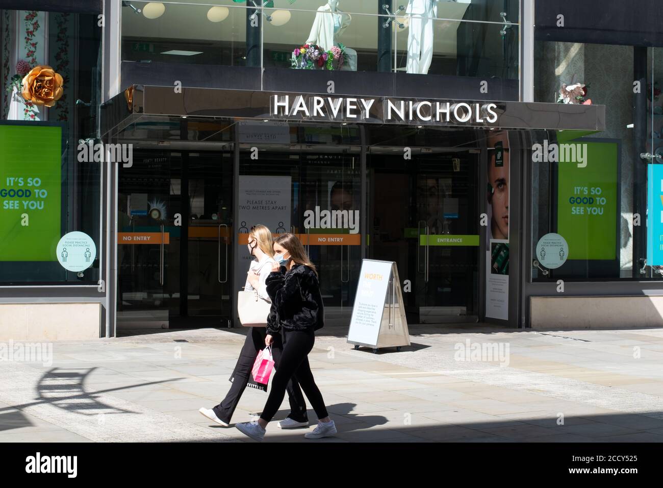 Ingresso al grande magazzino Harvey Nichols, Manchester UK, con due donne in maschere a piedi Foto Stock