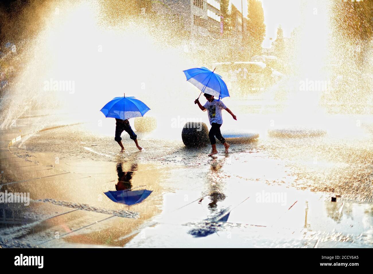Bambini con ombrelloni che camminano attraverso l'acqua, fontana a Karlsplatz, Città Vecchia, Monaco, alta Baviera, Baviera, Germania Foto Stock