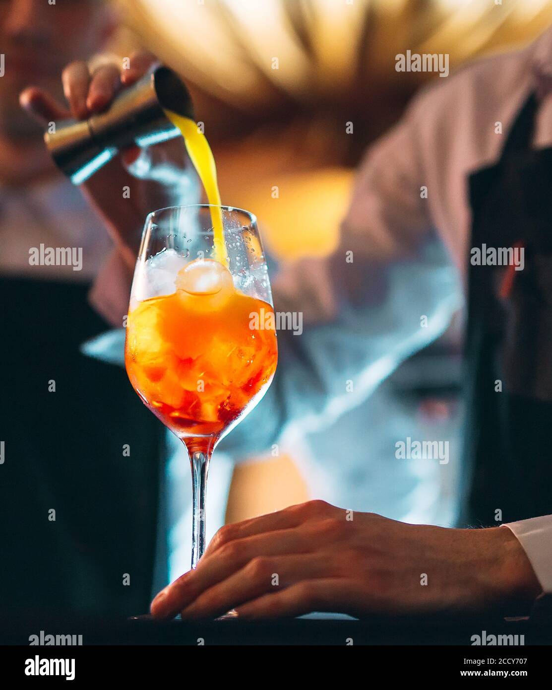 Barman mano che mescola un fresco e dolce cocktail estivo d'arancia con un cucchiaio al bancone del bar. Foto Stock