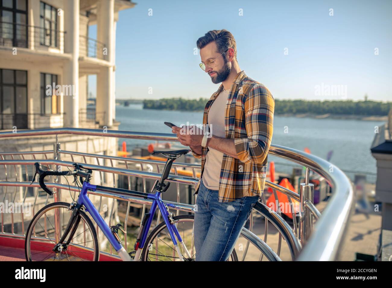 Uomo che guarda con attenzione nello smartphone vicino alla bicicletta Foto Stock