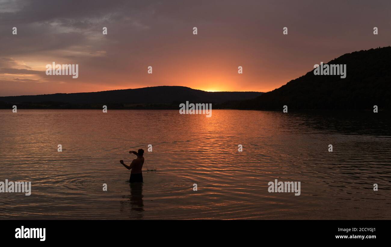 Un uomo che lancia pietre nel lago di Chalain, in Francia Foto Stock