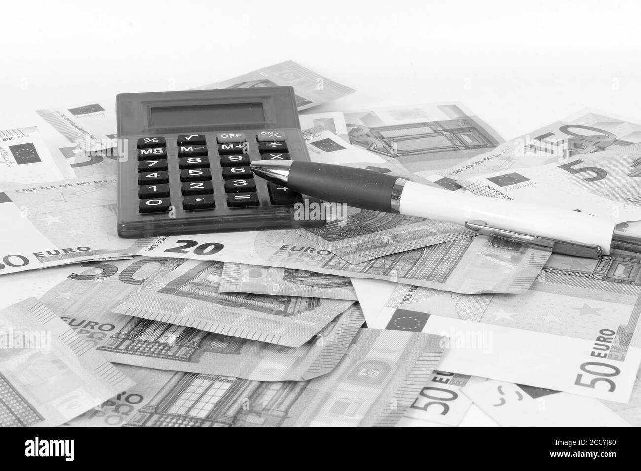 Scala di grigi di una pila di soldi con una calcolatrice e una penna a sfera sulla parte superiore Foto Stock