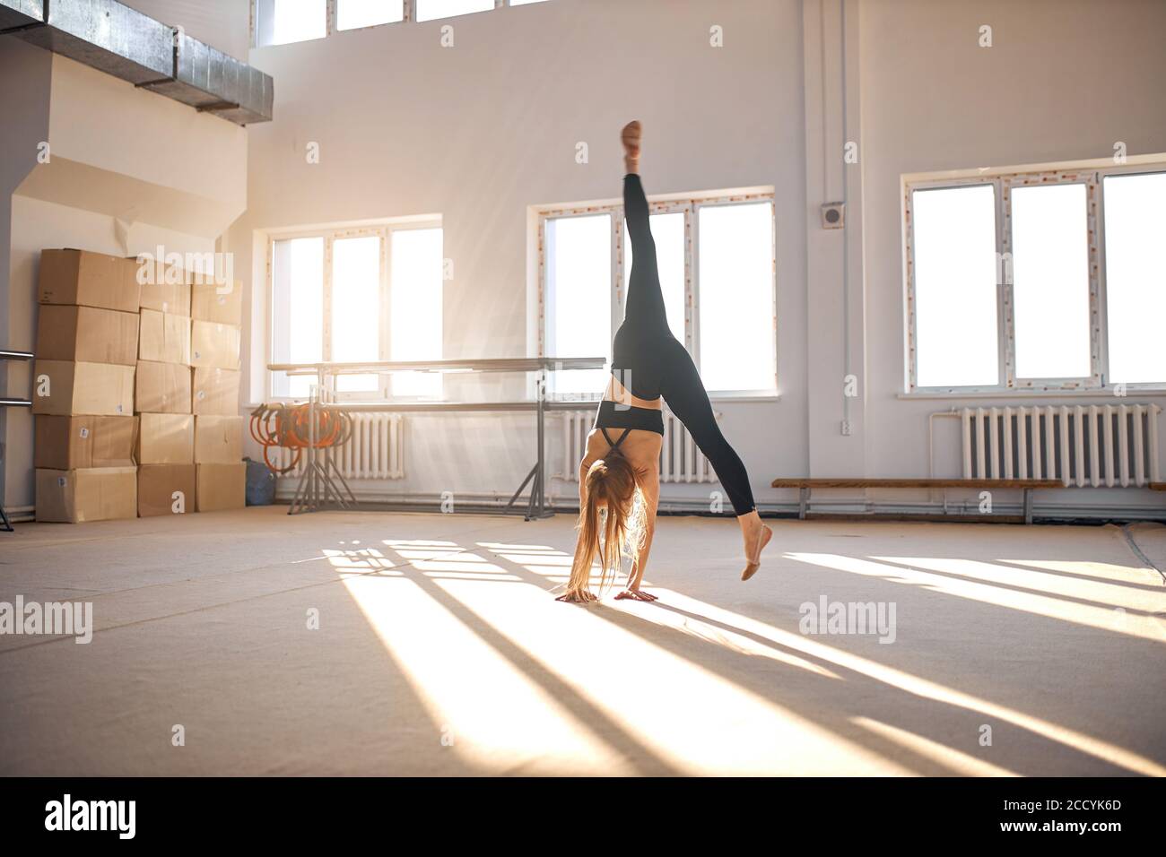Giovane donna di buona forma che esegue l'elemento di ginnastica d'arte, facendo il handstand in scuola di ginnastica, facendo split balzo in aria, sport e successo conce Foto Stock