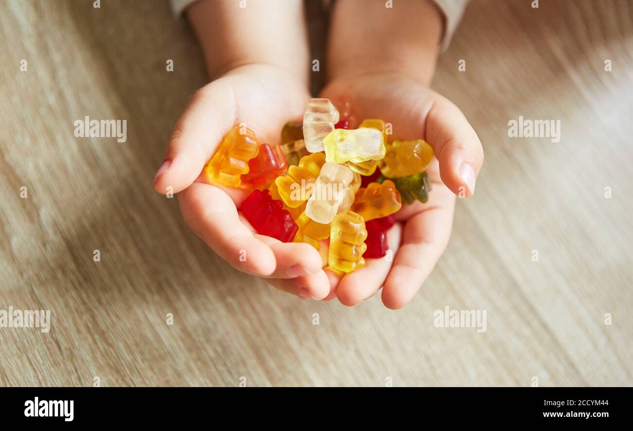 Le mani di un bambino tengono gli orsi gummy colorati come caramella per fare uno spuntino Foto Stock