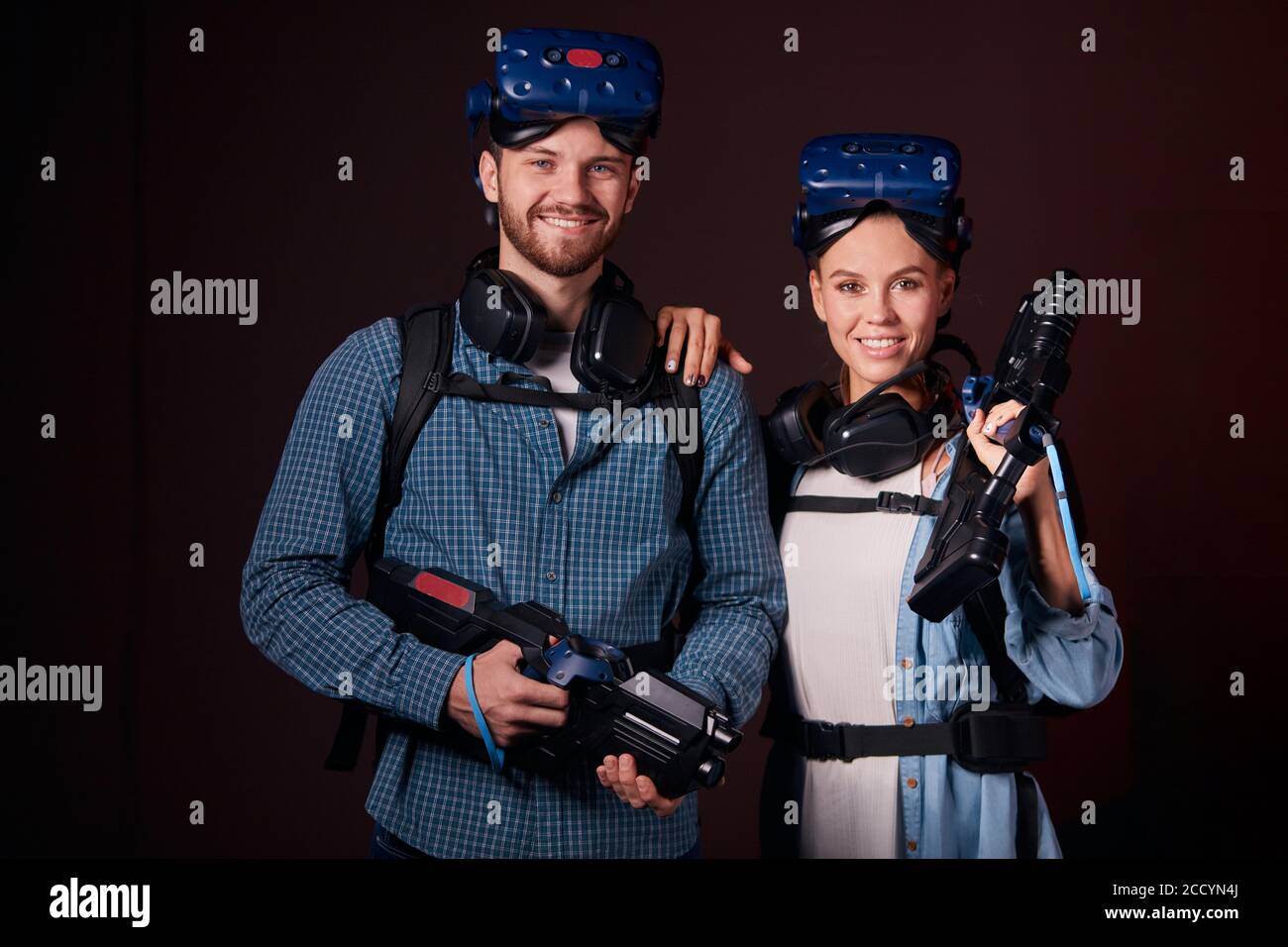 Giovane donna e uomo positivo con speciali dispositivi VR, arma e maschera sugli occhi guardare la telecamera e sorridere. Hi-tech, realtà virtuale, moderna Foto Stock