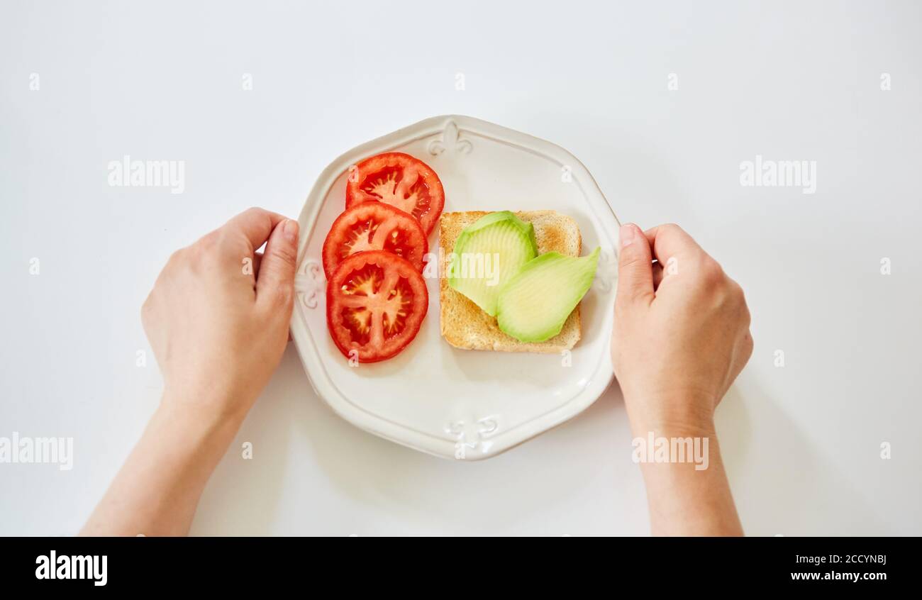 Due mani davanti al piatto con pane tostato con avocado e il pomodoro come uno spuntino sano Foto Stock