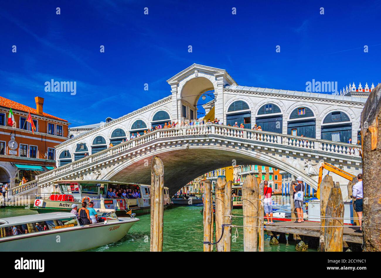 Venezia, Italia, 13 settembre 2019: Yacht e vaporetto navigano sulle acque del Canal Grande sotto il Ponte di Rialto, tipici edifici colorati e lo sfondo azzurro del cielo Foto Stock