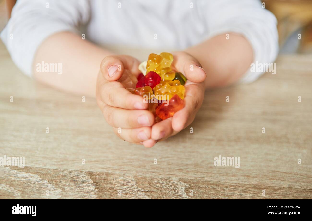 Il bambino tiene in mano molti orsacchiotti gummy colorati snacking Foto Stock