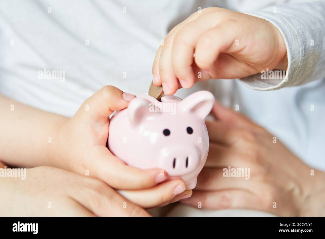 Mano di un bambino mette una moneta in piggy rosa banca come concetto di investimento Foto Stock