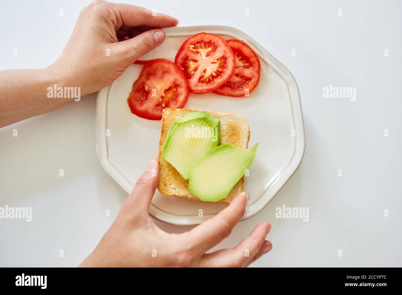 Due mani preparano il pane tostato con avocado e pomodoro Foto Stock