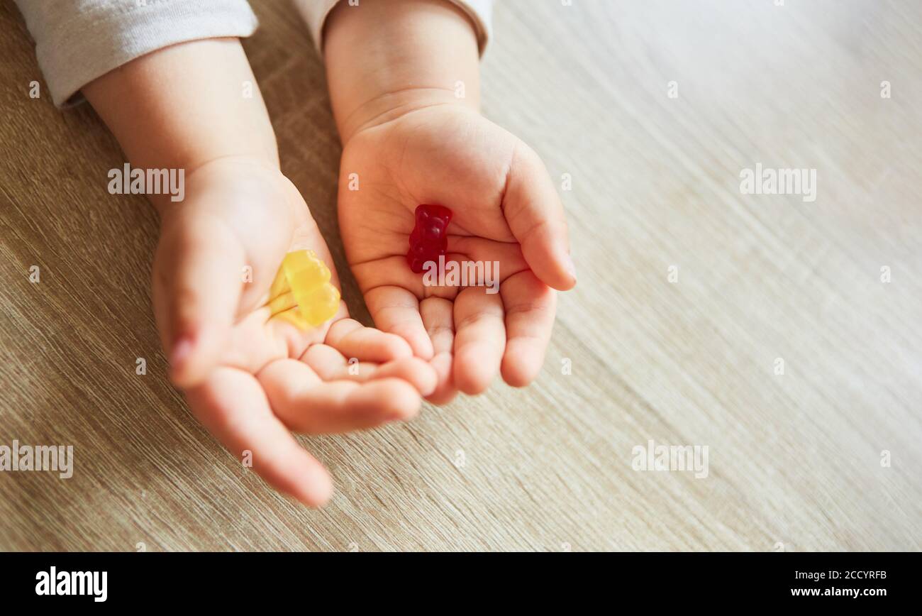 Il bambino tiene un orso gommoso in ogni mano come un caramelle tra cui scegliere Foto Stock