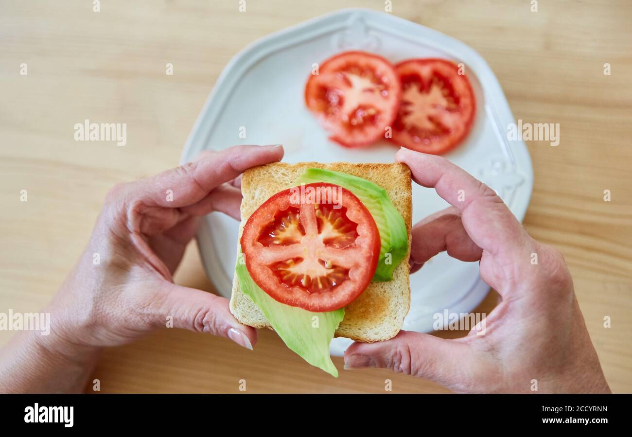 Le mani tengono un brindisi vegano con avocado e pomodoro come uno spuntino sano Foto Stock