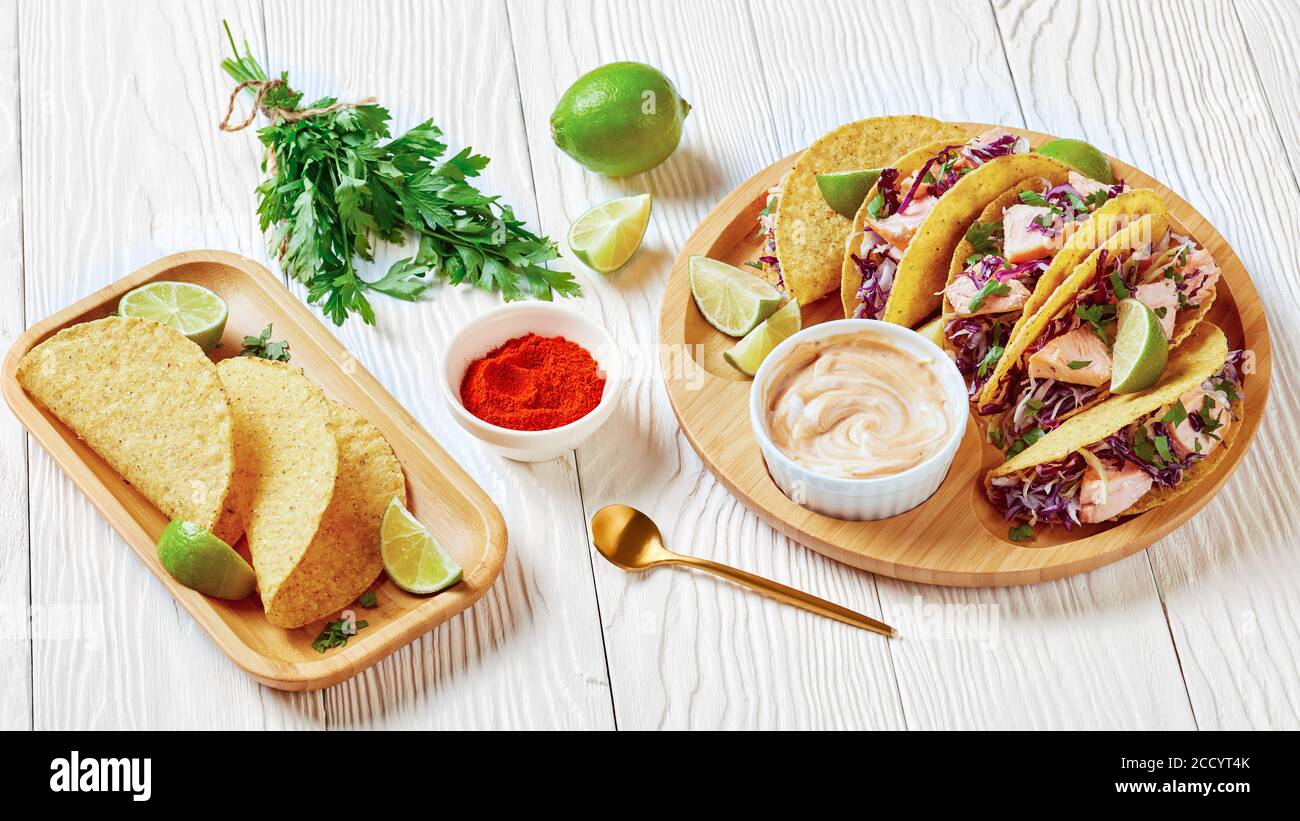 tacos di salmone con insalata di cavolo rosso con salsa piccante allo yogurt cosparsa di prezzemolo tritato finemente servito su un piatto di bambù su un tavolo di legno bianco, la Foto Stock