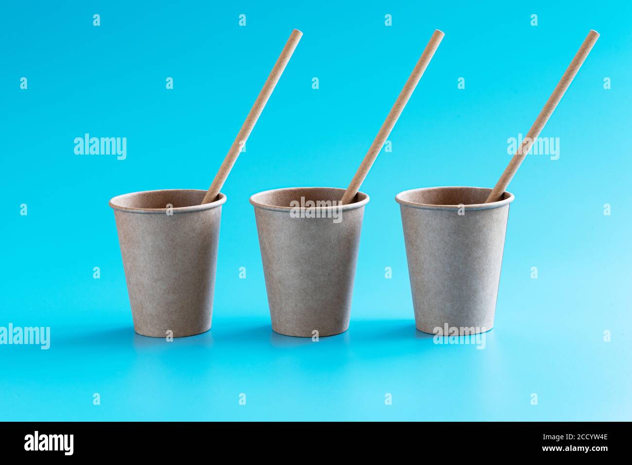Tre tazze di carta da mestiere marroni monouso con cannucce di carta in fila su sfondo blu. Stoviglie eco-compatibili. Concetto di riciclaggio. Tema zero rifiuti Foto Stock