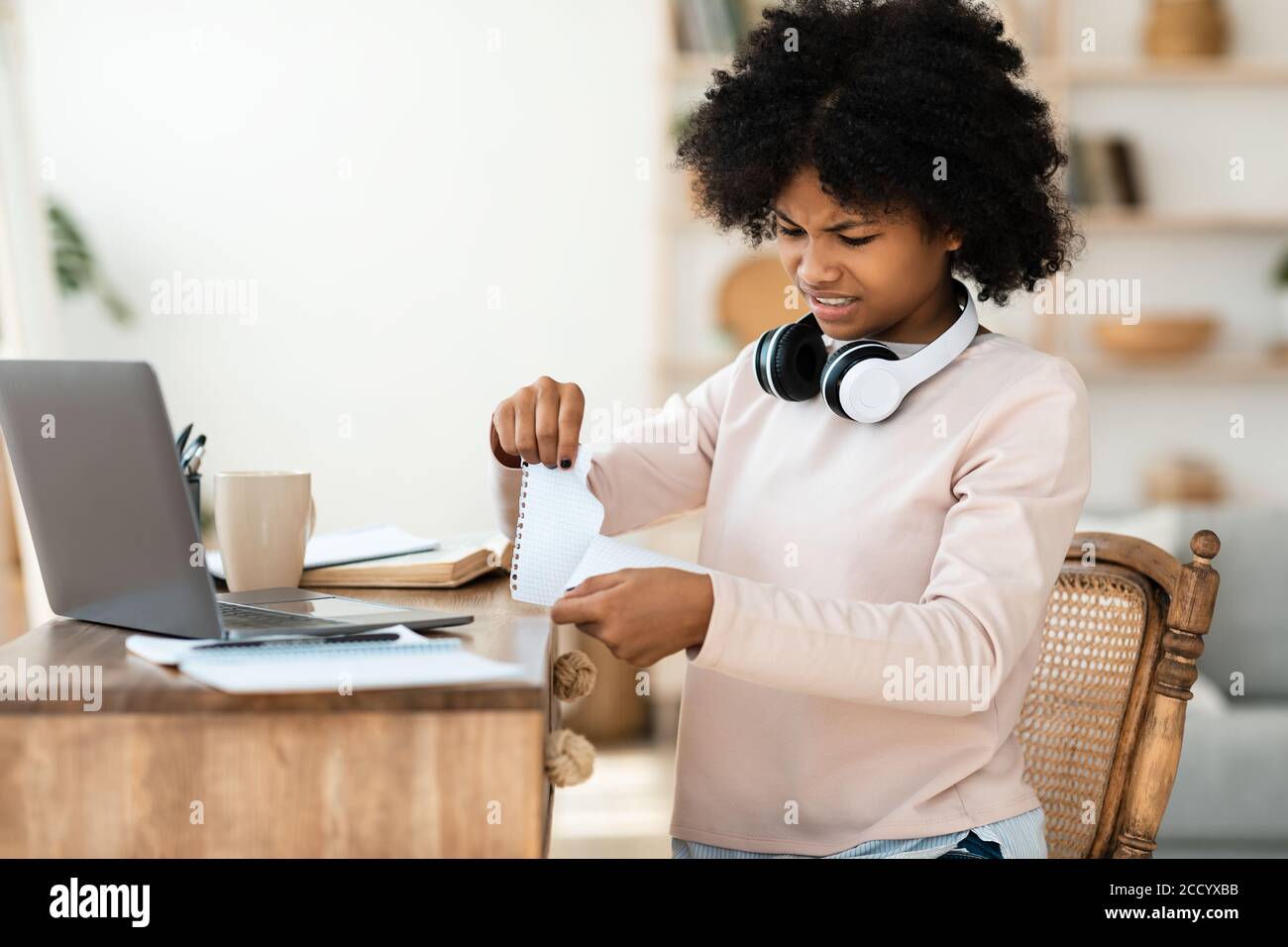 Teenager Girl Tearing pagina fuori dal lavoro Libro seduta all'interno Foto Stock