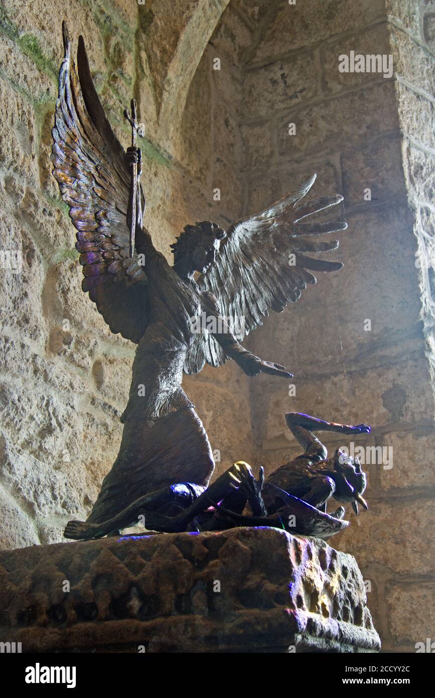 San Michele uccide Lucifero in una scultura in bronzo nella cappella del Monte San Michaels in Cornovaglia. La luce proveniente da una finestra in vetro colorato nelle vicinanze aggiunge fascino. SC Foto Stock