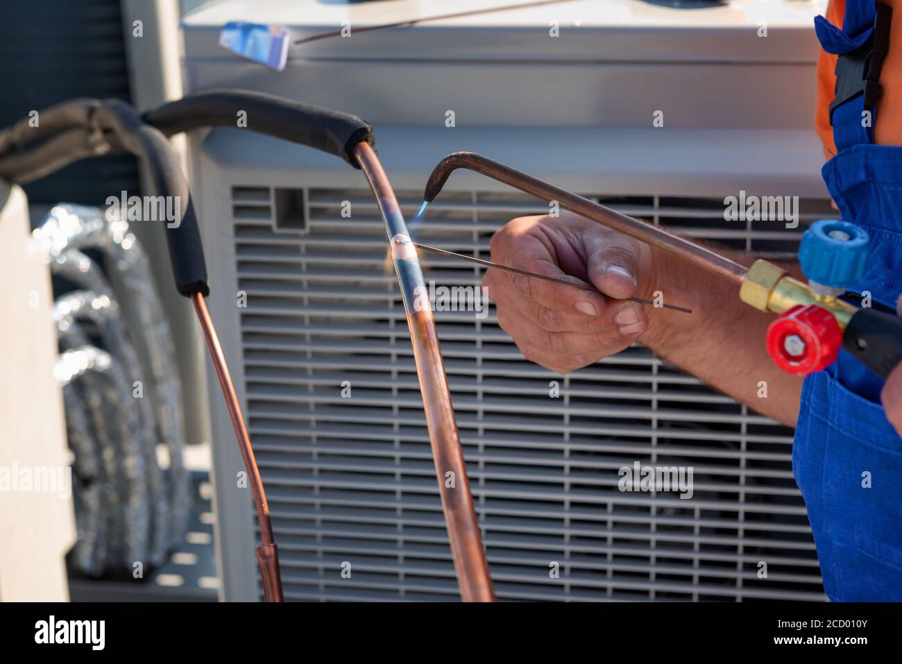 Il tecnico HVAC sta lavorando sulle unità di condizionamento dell'aria su un tetto di nuovo edificio industriale. Immagine a segmenti del tecnico HVAC che salda il giunto di rame Foto Stock