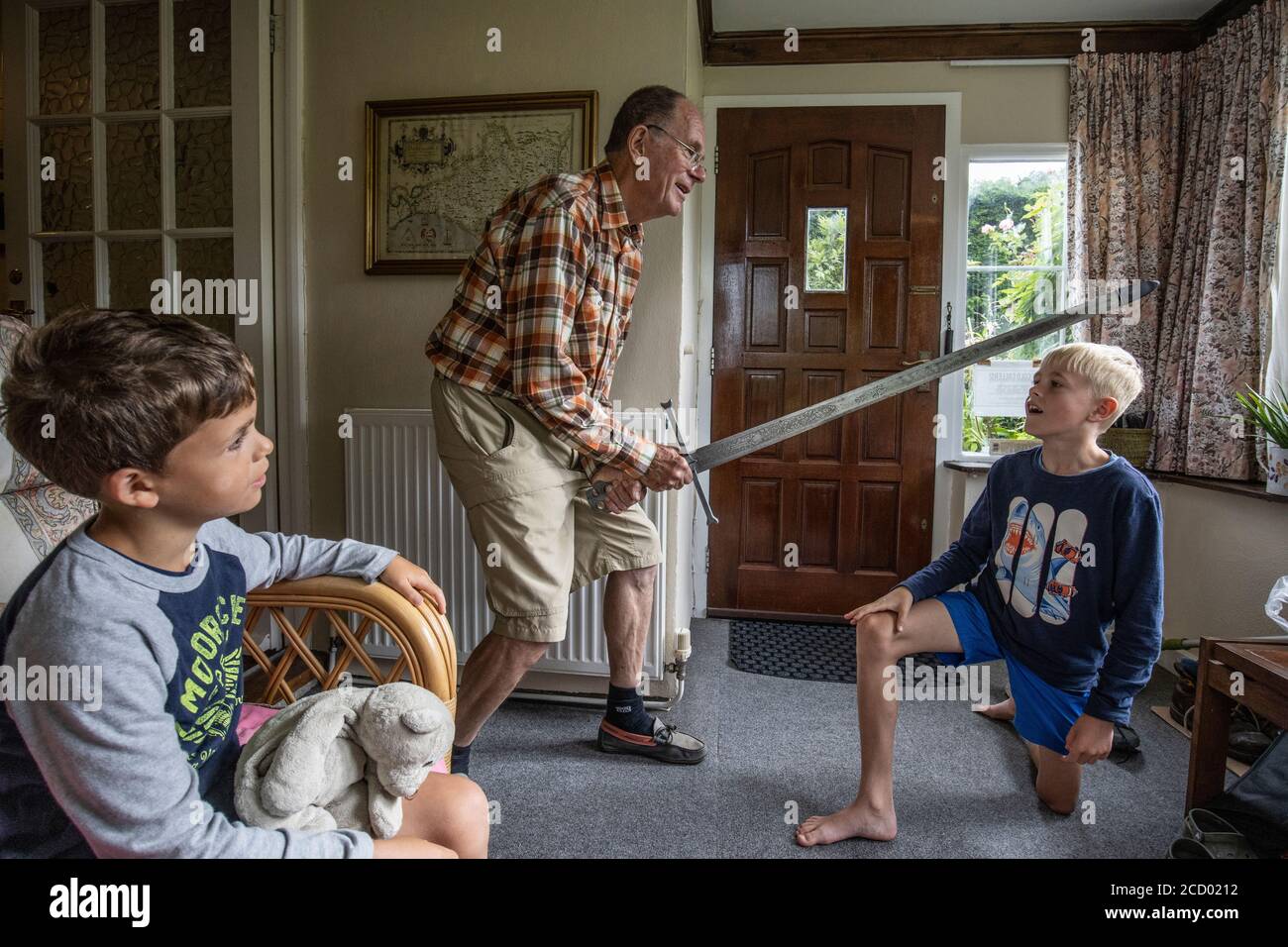 Nonno che gioca con i nipoti mentre tiene la storica spada metallica a casa, Galles, Regno Unito Foto Stock