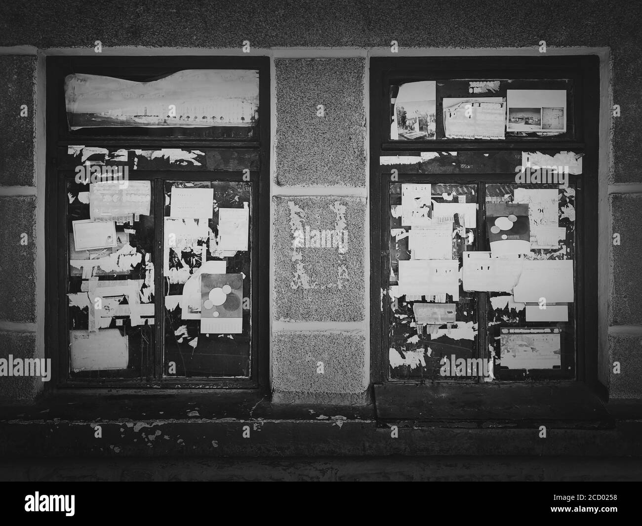 Fotografia di strada in bianco e nero, pubblicità graffiata su vecchie finestre. Poster urbani strappati sulla facciata di un edificio, cartelloni diversi sbriciolati Foto Stock