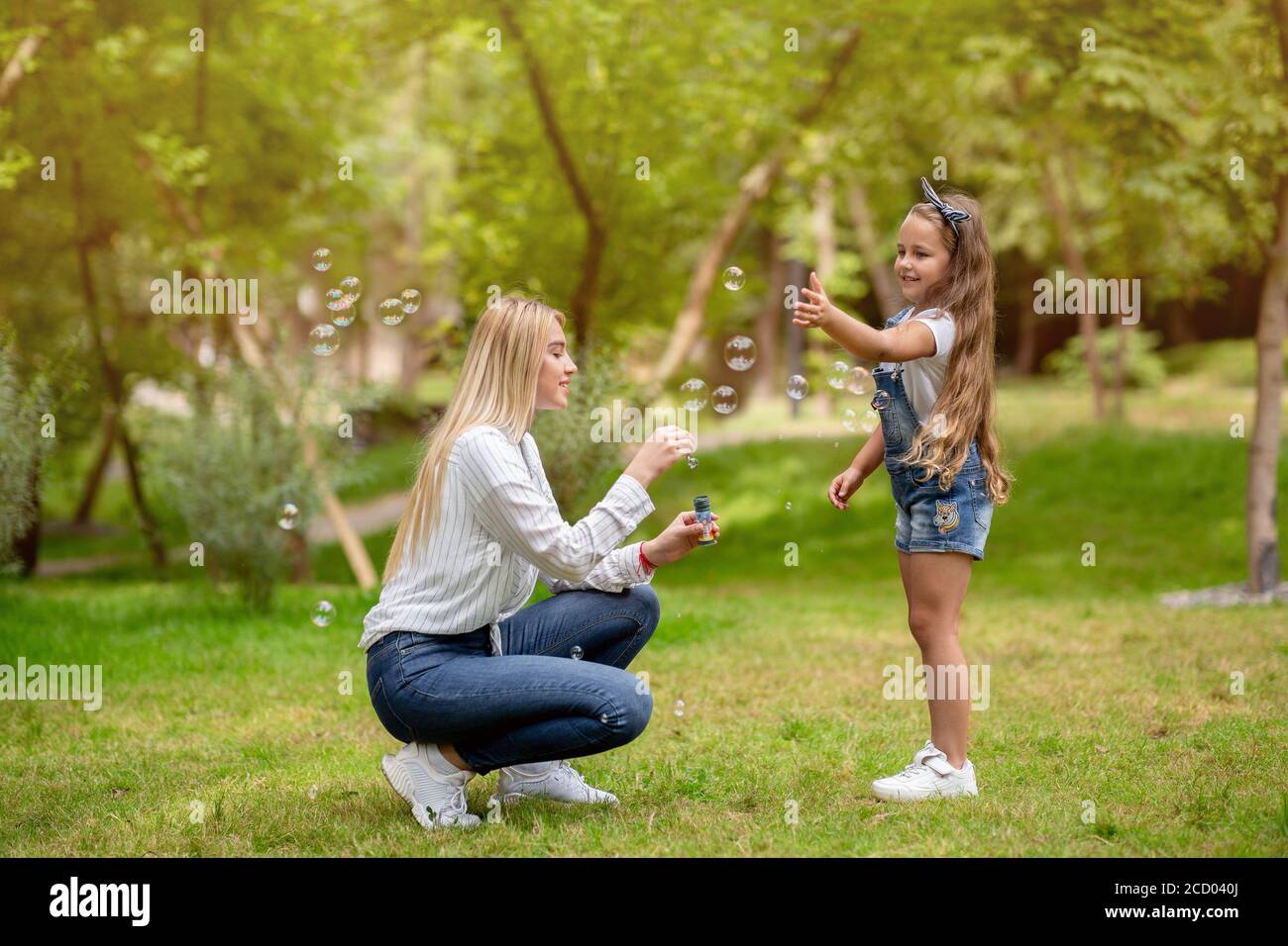 Madre e piccola figlia che si diverta con le bolle di sapone all'aperto Foto Stock