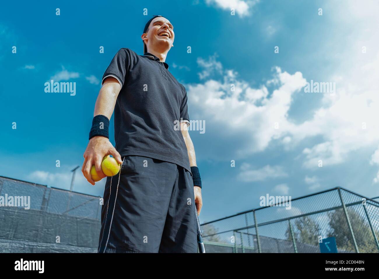 Primo piano di Young Attractive Man Laughung e relax dopo il torneo e tenendo palle e racchetta da tennis. Foto Stock