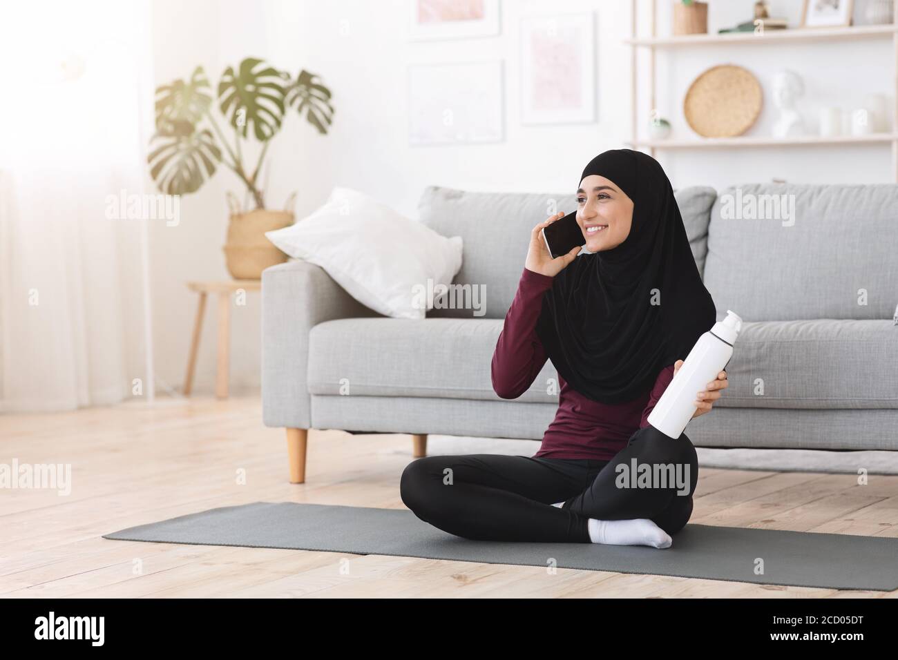 Donna araba felice in Hijab che parla su Cellphone dopo l'allenamento A casa Foto Stock