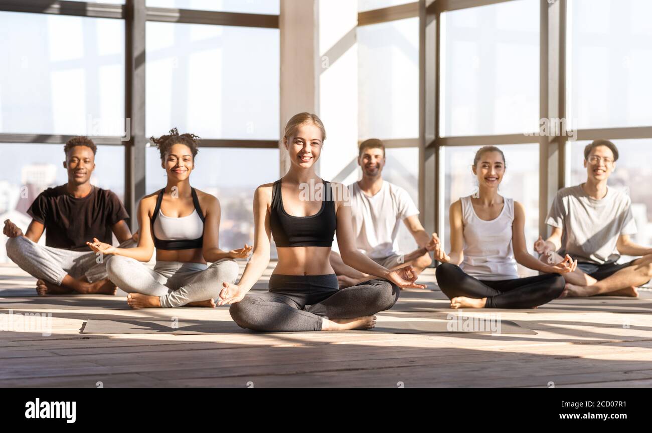 Gruppo internazionale di yoga che si pone in studio moderno durante l'allenamento di meditazione Foto Stock